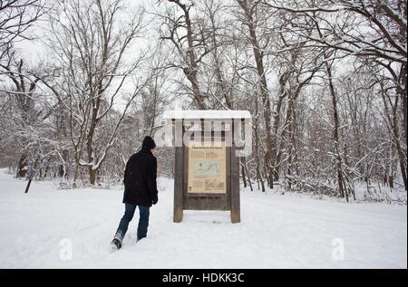 Ein Mann geht durch Schnee ein Schild mit einer Karte auf Hecht Insel, ein Teil von Fort Snelling Staatspark in Minneapolis. Stockfoto