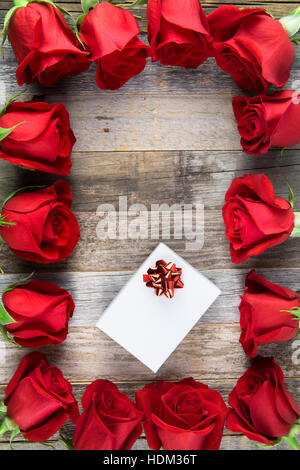 Rahmen von roten Rosen und weißen Geschenkbox auf Holzoberfläche. Stockfoto