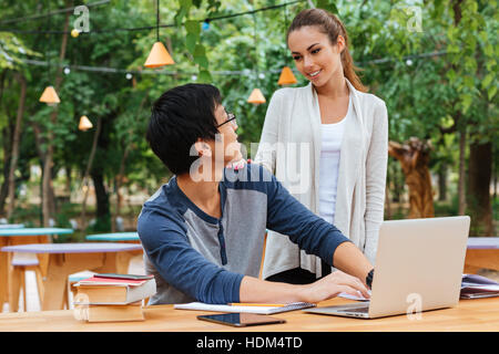 Lächelnd junges Paar sprechen und mit Laptop im freien Stockfoto