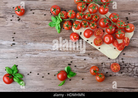 Tomaten und Paprika in Gruppen mit Blättern Basilikum auf dem braunen Holztisch. Stockfoto
