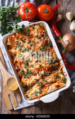 Mexikanische Enchilada in einer Auflaufform mit den Zutaten auf den Tisch. vertikale Ansicht von oben Nahaufnahme Stockfoto