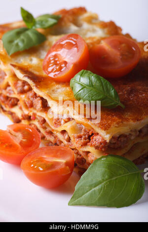 Ein Stück Lasagne mit frischem Basilikum und Tomaten auf einem weißen Teller. Vertikale Nahaufnahme Stockfoto