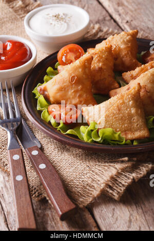 vegetarische Samosa Teigtaschen auf einem Teller mit Tomaten und Salat auf einem Holztisch. vertikale Stockfoto