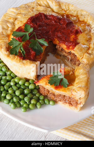 In Scheiben geschnittene Fleisch Pie und grüne Erbse auf einem Teller. Vertikale Nahaufnahme Stockfoto