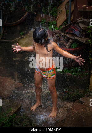 Ein junges Kind der kambodschanischen Khmer kühlt sich im Regenwasser gießen aus einem Fallrohr in Siem Reap, Kambodscha. Stockfoto