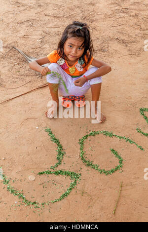 Ein fünfjährige kambodschanisches Mädchen lernt ihr Khmer-Alphabet mit zerrissenen Stücke der Blätter in den Schmutz in Kambodscha angeordnet. Stockfoto