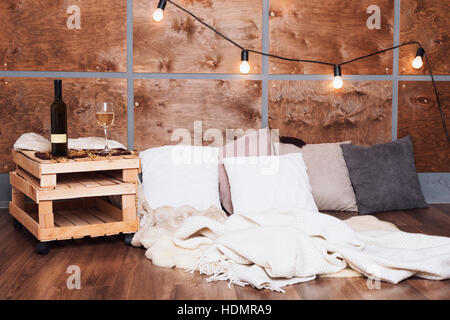 Glas Weißwein und Flasche im modernen Loft-Innenraum mit Licht Girlande auf Holzwand. Stockfoto
