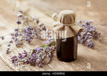 ätherisches Öl in einer Glasflasche, frischem Lavendel auf einem alten hölzernen Hintergrund Stockfoto