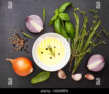 Olivenöl mit Gewürzen, Kräutern und Gemüse auf dem schwarzen Schiefer Hintergrund Stockfoto