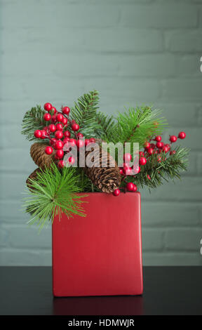 Immergrün, Beeren und Zapfen in einem leuchtend roten Topf. Sehr realistische Dekoration. Stockfoto