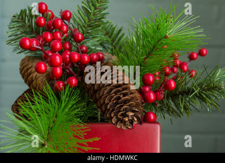 Immergrün, Beeren und Zapfen in einem leuchtend roten Topf. Sehr realistische Dekoration, zentriert. Stockfoto