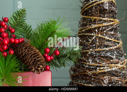 Immergrün, Beeren und Zapfen in einem leuchtend roten Topf mit einer abstrakten Baumschmuck. Enger Foto. Stockfoto