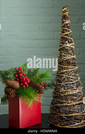 Immergrün, Beeren und Zapfen in einem leuchtend roten Topf mit einer abstrakten Baumschmuck. Im Hochformat. Stockfoto