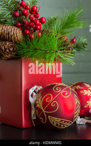 Immergrün, Beeren und Zapfen in einem leuchtend roten Topf mit aufwendigen dekorativen Weihnachtsschmuck. Enger Foto. Stockfoto