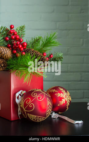 Immergrün, Beeren und Zapfen in einem leuchtend roten Topf mit aufwendigen dekorativen Weihnachtsschmuck. Stockfoto