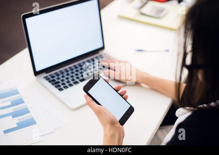 Frauenhand mit Handy und Laptop im Büro Stockfoto