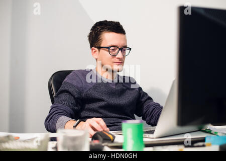 Anstrengenden Arbeitstag. Gut aussehend nachdenklicher junger Mann mit Brille auf Laptop sitzend an seinem Arbeitsplatz Stockfoto