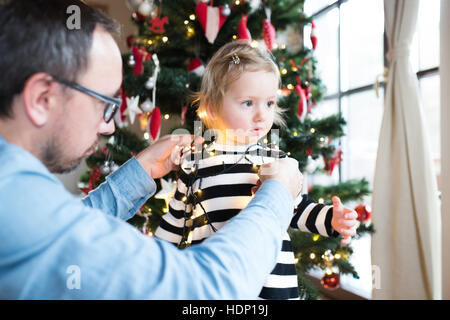 Vater mit stahlharte verstrickt in Lichterkette am Weihnachtsbaum. Stockfoto