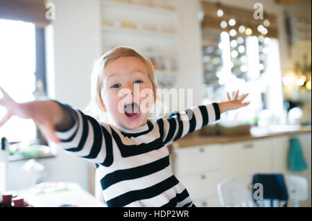 Niedliche kleine Mädchen im gestreiften Kleid sitzt am Küchentisch, shou Stockfoto