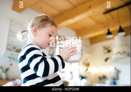 Niedliche kleine Mädchen im gestreiften Kleid sitzt am Küchentisch, halten Stockfoto