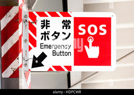 Bahnhof Zeichen in Japanisch und Englisch. Rot und Weiß, mit Symbol Hand drücken der Taste, markiert die OS', dann Pfeil nach Not-Aus-Knopf. Stockfoto