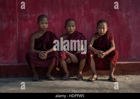 Drei junge buddhistische Mönche gegen eine rote Wand des Shwe Yan Pyay Klosters in Nyaungshwe, Myanmar. Stockfoto