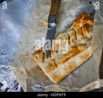 Apfelstrudel hausgemachte Kuchen mit Äpfeln und Zimt, mit einem Messer liegen auf Tischdecke aus Baumwolle von Hand auf dem Küchentisch eingerichtet geschnitten Stockfoto