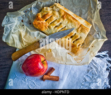 Apfelstrudel hausgemachte Kuchen mit Äpfeln und Zimt, mit einem Messer liegen auf Tischdecke aus Baumwolle von Hand auf dem Küchentisch eingerichtet geschnitten Stockfoto