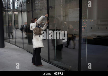 Eine Frau benutzt ihr Smartphone zu eine corporate Foyer Interieur, fotografieren ihr Handy scheinbar gemischt mit der Architektur des Gebäudes, am 9. Dezember 2016, in der City of London. Stockfoto