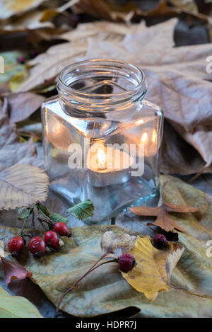 Glas mit Kerze zwischen trockenen Blätter Stockfoto