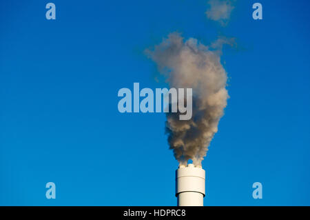 Es werden verschmutzte Rauch vor einem strahlend blauen Himmel aus dem hohen Schornstein Stockfoto