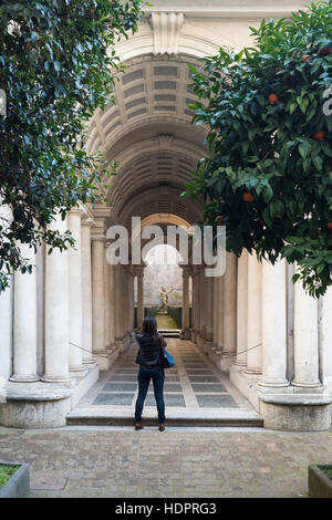 Rom. Italien. Person auf der Suche nach Francesco's Borromini 17 C Trompe l'oeil gezwungen Perspektive Kolonnade Galerie im Innenhof des Palazzo Spada. Stockfoto