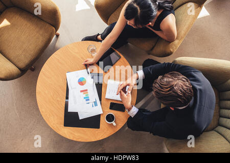 Draufsicht der Geschäftskollegen mit Diagramme während der Gesellschafterversammlung am Tisch sitzen. Unternehmer und Unternehmerin diskutieren neues Projekt während sitti Stockfoto