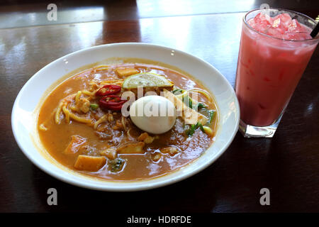 Eine Schüssel mit Nudeln Curry Laksa, eine Malaysier authentischen Gericht mit einem Glas milchig Rose Wasser Sirup Getränk namens Air Bandung Stockfoto