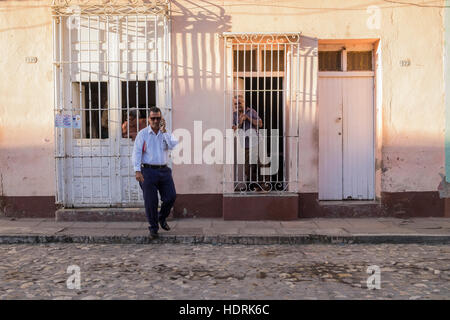 Mann auf dem Handy geht weg von Haus mit typischen vergitterten Fenstern in Trinidad, Kuba Stockfoto