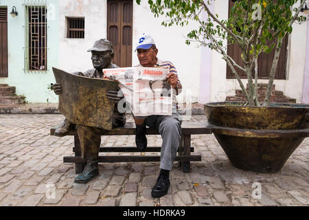 Mann sitzt liest eine Zeitung neben einer Bronze-Skulptur von ihm lesen eine Zeitung von Künstlerin Martha Jimenez in der Plaza del Carmen, Camagüey, Kuba Stockfoto