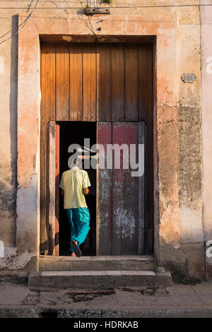 Mann betritt sein Haus durch eine alte hölzerne Eingangstür getaucht in warmes Sonnenlicht, Camagüey, Kuba Stockfoto