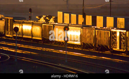 Orange Abendlicht spiegelt sich die glänzende Seite eines Güterzuges in Barstow, CA. Hinweis rot Eisenbahn Signal Warnleuchten. Stockfoto