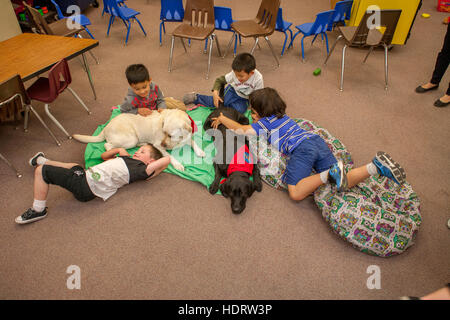 Gemischtrassige junge Studenten umarmen einen Therapiehund auf dem Boden eines Grundschule Klassenzimmer in Mission Viejo, Kalifornien. Stockfoto