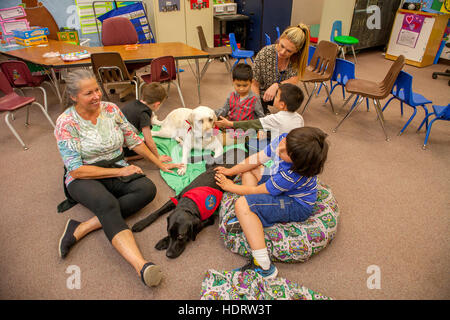 Gemischtrassige junge Studenten umarmen einen Therapiehund auf dem Boden eines Grundschule Klassenzimmer in Mission Viejo, CA. Hinweis Lehrerin und Mutter. Stockfoto