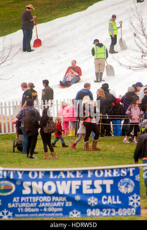 Einheimischen Schlitten hinunter einen Hügel künstlich beschneit bei einer Winter-Karneval "Snowfest' in Lake Forest, CA. Hinweis Arbeiter mit Schaufeln. Stockfoto