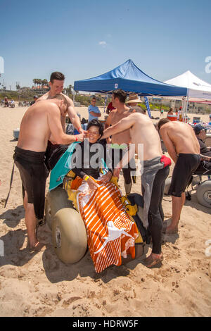 Lokalen Gönnern verleihen einer behinderte Frau militärischen Veteran in einen Neoprenanzug vor einen Surfkurs in Huntington Beach, CA. Hinweis Oversize Reifen für die Navigation auf Sand und Baldachin im Hintergrund eine Anwendung von Sonnenschutzmitteln. Stockfoto