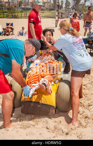 Lokalen Gönnern verleihen einer behinderte Frau militärischen Veteran in einen Neoprenanzug vor einen Surfkurs in Huntington Beach, CA. Hinweis Oversize Reifen für die Navigation auf Sand und Baldachin im Hintergrund eine Anwendung von Sonnenschutzmitteln. Stockfoto