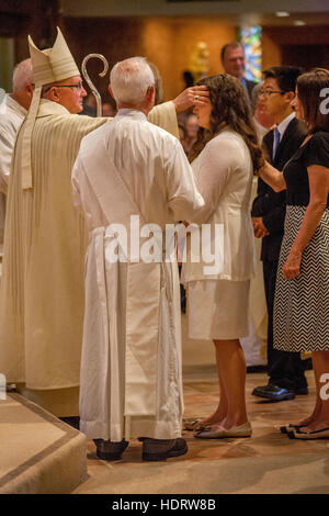 Von ihren Eltern begleitet, beteiligen formal gekleidete Jugendliche sich Bestätigung Messe in Laguna Niguel, CA, katholische Kirche vor einem wogenden Bischof. Stockfoto