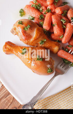 Roasted Chicken Drumsticks und karamellisierten Baby-Karotten auf einer Platte Nahaufnahme. vertikale Ansicht von oben Stockfoto
