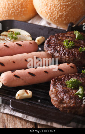 gegrillte Burger und Würstchen mit Zwiebel und Knoblauch auf dem Grill hautnah. vertikale Stockfoto