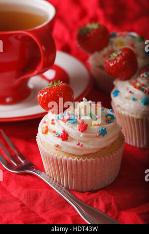 Schönen Cupcakes mit Sahne und frischen Erdbeeren und eine Tasse Tee auf dem Tisch. vertikale Nahaufnahme Stockfoto