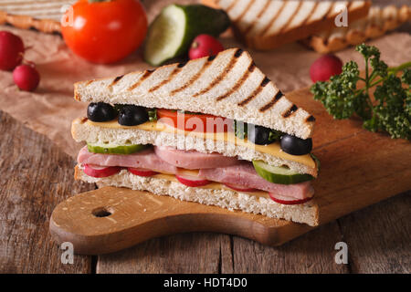 Sandwich mit Schinken, Käse und Gemüse auf dem Schneidebrett und Zutaten auf den Tisch. horizontale Stockfoto