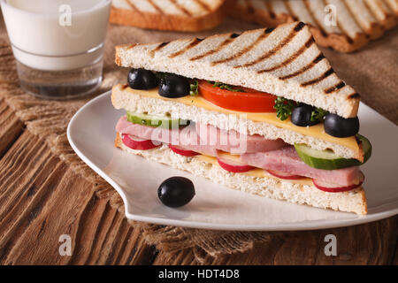 Sandwich mit Schinken und Gemüse auf dem Teller und Milch auf dem Tisch. horizontale Stockfoto