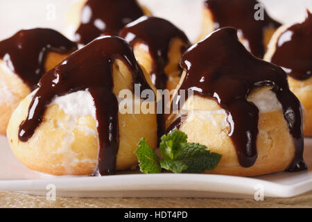 Frischen Windbeutel mit Sahne und Schokolade Zuckerguss auf einer Platte Makro. horizontale Stockfoto